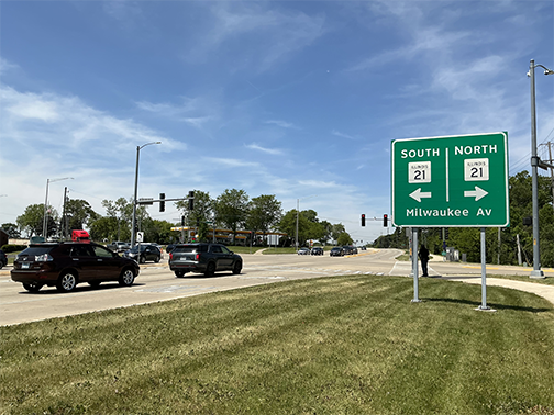 North and south Milwaukee Av sign in grass with road behind